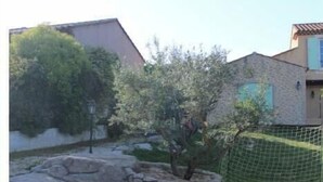 A sandy outdoor area with a tree, a fence, and a building in the background. - Charming air-conditioned studio with pool between Aix-en-Provence and Marseille (Les Pennes-Mirabeau)