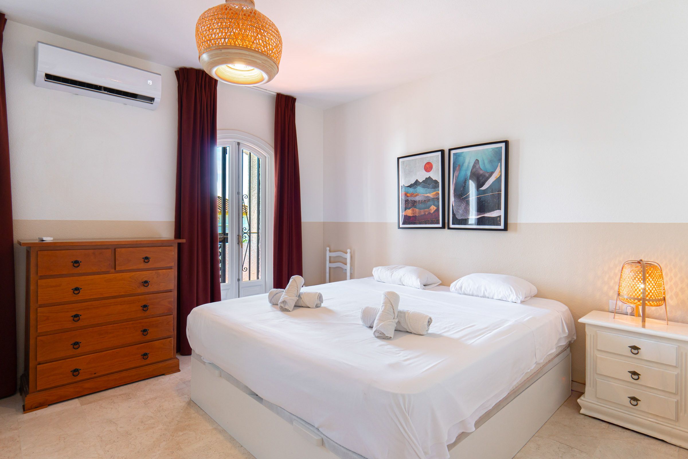 A hotel room with a bed, a dresser, a nightstand, and two wall-mounted artworks.