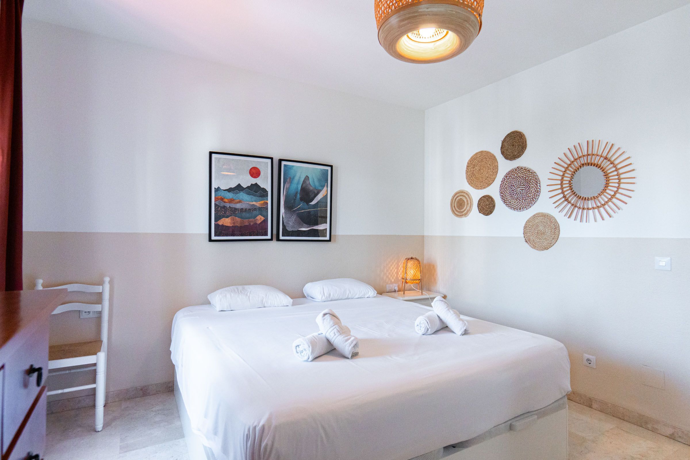 A hotel room with a bed, two framed artworks, a wall-mounted light fixture, and a wall decoration.