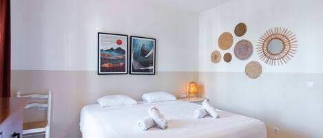 A hotel room with a bed, two framed artworks, a wall-mounted light fixture, and a wall decoration.