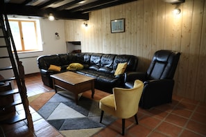 A living room with a black leather sofa, a wooden coffee table, a yellow armchair, a black leather chair, and a patterned rug.