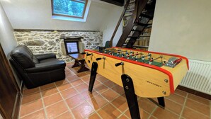 A room with a foosball table, a leather sofa, a stone wall, a window, and a bookshelf. - The Otter Cottage! Vacation Rental with Indoor Pool; Chancelade Pond 500 meters away (Charensat)