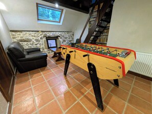A room with a foosball table, a leather sofa, a stone wall, a window, and a bookshelf. - The Otter Cottage! Vacation Rental with Indoor Pool; Chancelade Pond 500 meters away (Charensat)