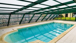 An indoor swimming pool with a clear glass bottom, surrounded by a tiled floor and a stone wall. - The Otter Cottage! Vacation Rental with Indoor Pool; Chancelade Pond 500 meters away (Charensat)