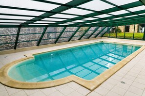 An indoor swimming pool with a clear glass bottom, surrounded by a tiled floor and a stone wall. - The Otter Cottage! Vacation Rental with Indoor Pool; Chancelade Pond 500 meters away (Charensat)