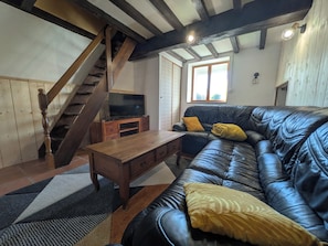 A living room with a wooden staircase, a leather sofa, a wooden coffee table, and a television on a stand. - The Otter Cottage! Vacation Rental with Indoor Pool; Chancelade Pond 500 meters away (Charensat)