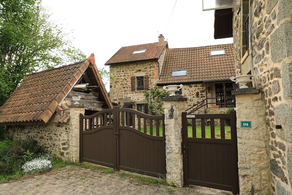 A stone building with a traditional tiled roof, a gated entrance, and a small garden area.