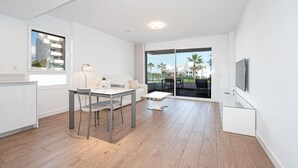 A modern apartment with a dining area, a sofa, a TV, and a balcony with a view of palm trees. - Luxury Pool View Isea 1111 (Torrox)