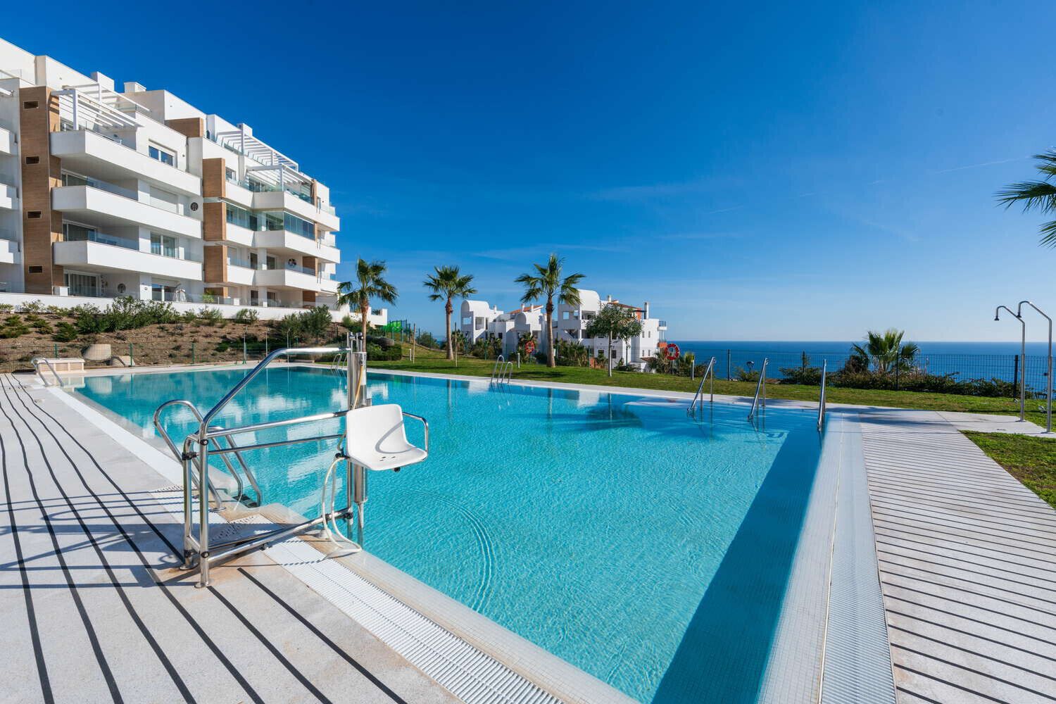 A swimming pool with a wooden deck, a lifeguard chair, and a view of the ocean.