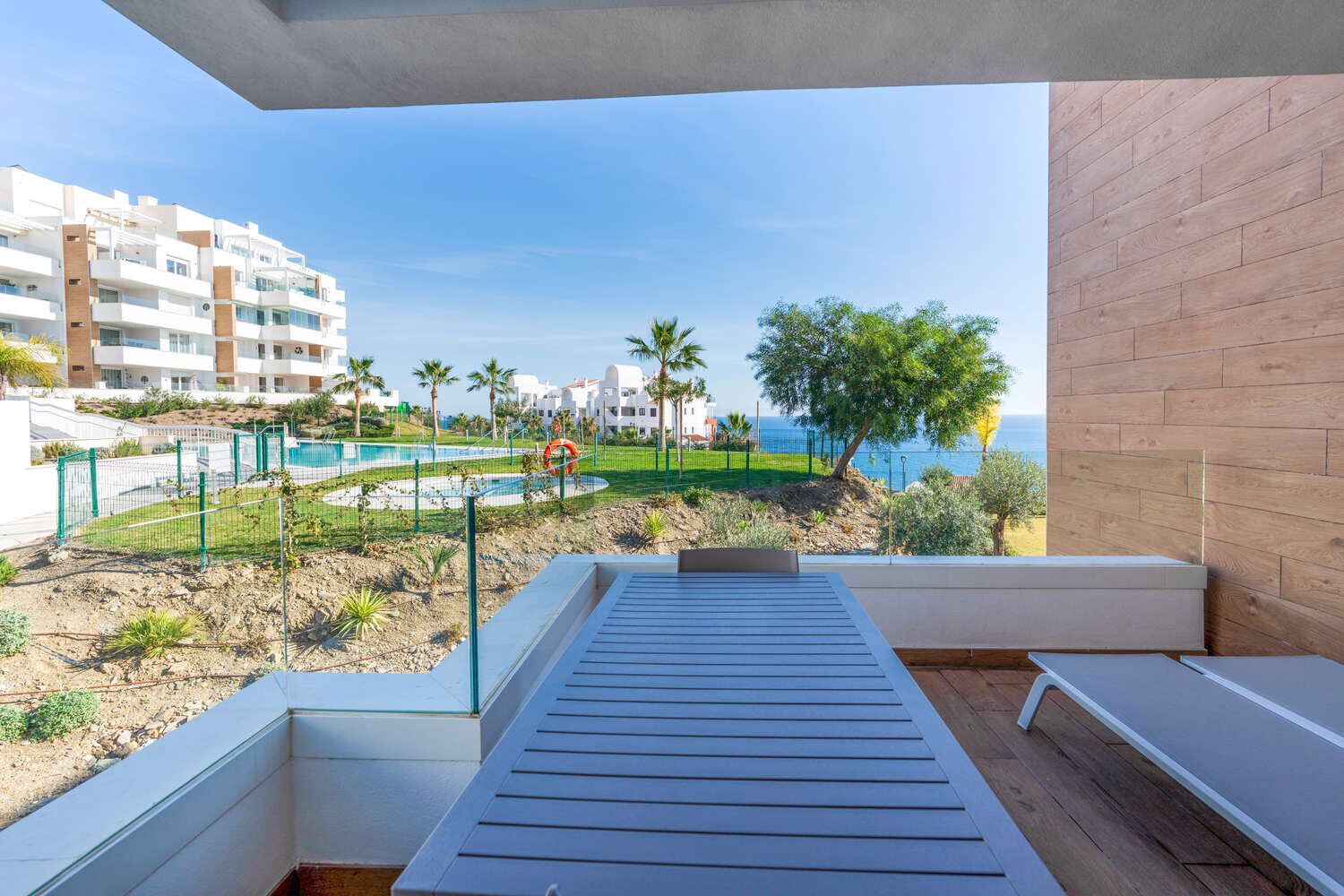 Un balcon donnant sur une piscine, des palmiers et un bâtiment en arrière-plan.