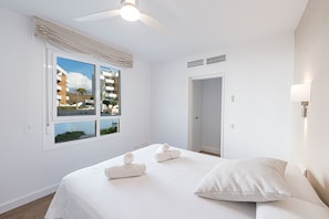 Una habitación de hotel con cama, ventilador de techo, ventana con vista a edificios y puerta.