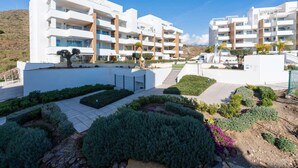 A modern multi-story building with balconies, a landscaped courtyard, and a hilly landscape in the background. - Luxury Pool View Isea 1111 (Torrox)