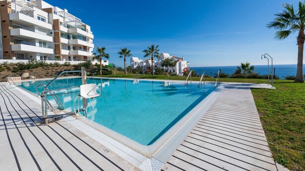 A swimming pool with a wooden deck, surrounded by palm trees and a clear blue sky. - Luxury Pool View Isea 1111 (Torrox)
