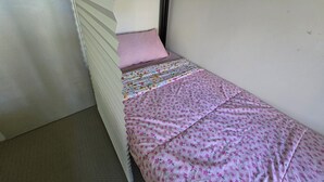 A single bed with a pink floral bedspread and a colorful quilt, a white headboard, and a plain wall. - Book a Bed in 4 Beds Mixed Dormitory (Ashcroft)