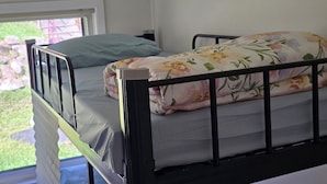 A single bed with a floral bedspread and a pillow, a window with a view of greenery, and a white wall. - Book a Bed in 4 Beds Mixed Dormitory (Ashcroft)