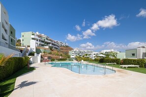 A swimming pool with a curved design, surrounded by a paved area with lounge chairs and a well-maintained lawn. - RDR544 - Stunning 2 Bedroom Apartment in Ipanema Homes (Mijas)