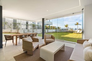 Ein modernes Interieur mit Essbereich, Sitzgelegenheiten und einer großen Glaswand mit Blick auf einen gepflegten Rasen und entfernte Gebäude.