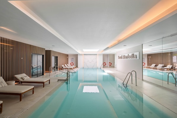 Ein moderner, überdachter Pool mit Liegestühlen, einer Glaswand und einem Schild mit der Aufschrift 'Soul Marbella'.
