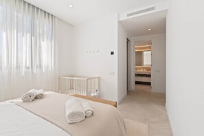 Ein modernes Hotelzimmer mit einem großen Bett, einem Babybett und einem durch eine offene Tür einsehbaren Badezimmer.
