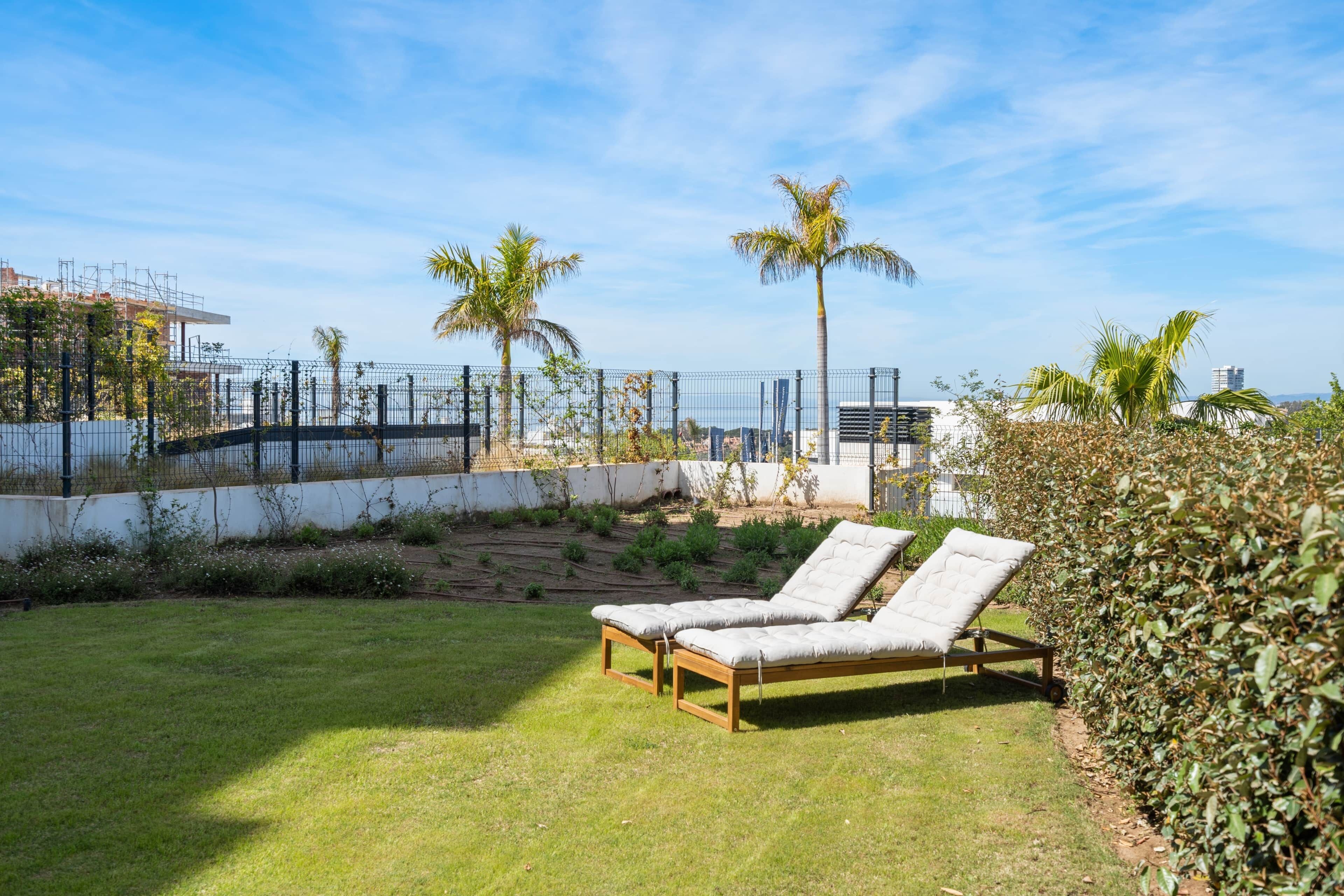 A grassy outdoor area with a lounge chair, palm trees, and a fence.