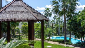 A thatched-roof gazebo, a swimming pool, and palm trees. - RDR541 - Gorgeous 2 bed Apt. in Los Flamingos (Marbella)