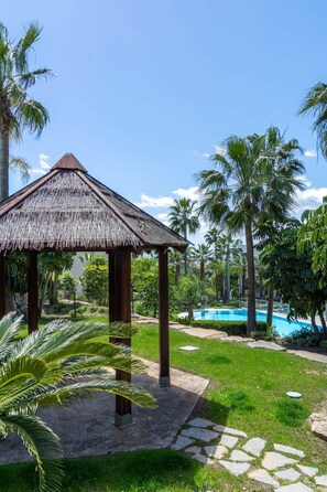 A thatched-roof gazebo, a swimming pool, and palm trees. - RDR541 - Gorgeous 2 bed Apt. in Los Flamingos (Marbella)