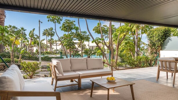 An outdoor seating area with a sofa, a small table, and a chair, surrounded by a fence and palm trees. - RDR541 - Gorgeous 2 bed Apt. in Los Flamingos (Marbella)