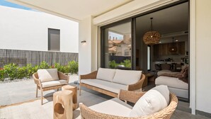 Un patio moderno al aire libre con mobiliario de mimbre, una puerta de cristal que da a la cocina y vistas de los edificios circundantes.