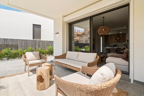 Eine moderne Außenpatio mit Korbmöbeln, einer Glastür, die zu einer Küche führt, und Blick auf die umliegenden Gebäude.