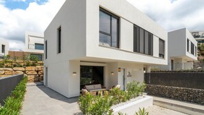 Una casa moderna de dos pisos con techo plano, ventanas amplias y un muro de contención de piedra.