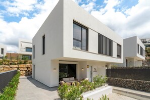 Ein modernes, zweistöckiges Haus mit Flachdach, großen Fenstern und einer steinernen Stützmauer.