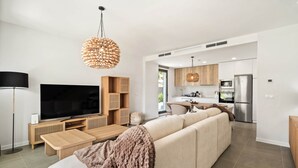 Una sala de estar moderna con un televisor de pantalla plana grande, un sofá, una mesa de centro y una zona de cocina con refrigerador y estufa.