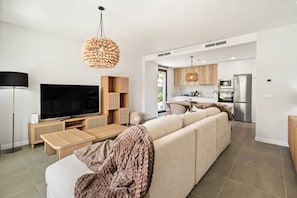 Ein modernes Wohnzimmer mit großem Flachbildfernseher, einer Couch, einem Couchtisch und einer Küchenzeile mit Kühlschrank und Herd.