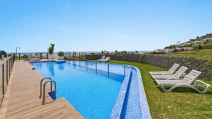 Una piscina con muelle de madera, sillas de descanso y pared de piedra.