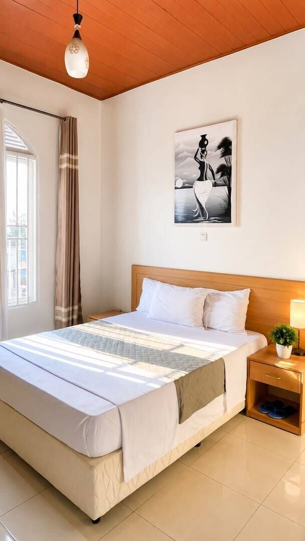 Ein Hotelzimmer mit Bett, Nachttisch, Lampe und einem Fenster mit Vorhängen.