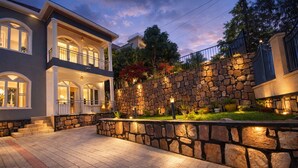 A two-story house with a stone wall and a paved driveway.