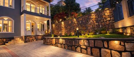 A two-story house with a stone wall and a paved driveway.