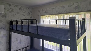 A bunk bed room with floral wallpaper, a window with blinds, and a ceiling fan.