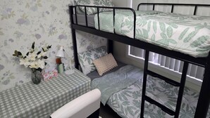 A bunk bed room with floral wallpaper, a small table with a checkered tablecloth, and a vase with flowers.