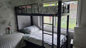 A bunk bed room with a checkered table, a lamp, and a window with a view of the outside.