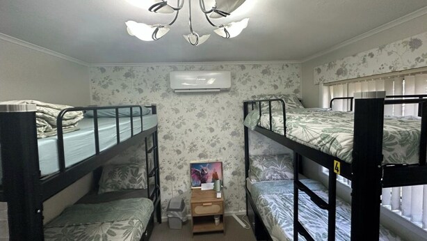 A dormitory room with bunk beds, a ceiling fan, an air conditioning unit, and a small desk with a chair.