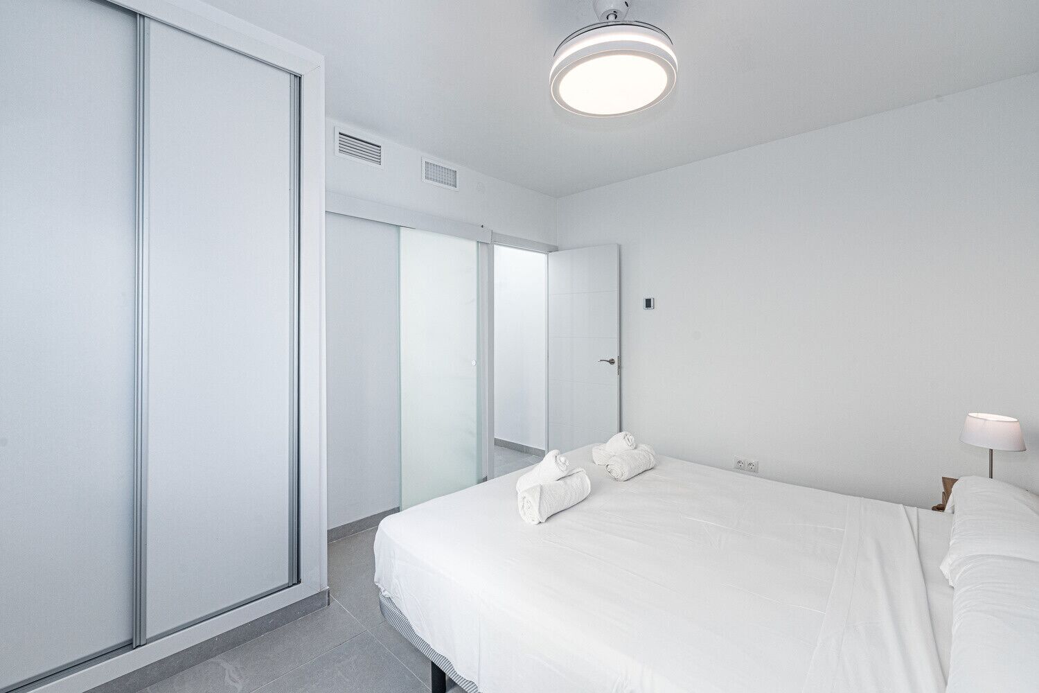 Ein modernes Hotelzimmer mit einem großen Bett, einem Nachttisch, einer Lampe und einem Kleiderschrank.