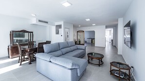 A modern living room with a grey sectional sofa, a wooden dining table with chairs, a glass coffee table, and a TV mounted on the wall. - Paloma Central Apartment (Nerja)