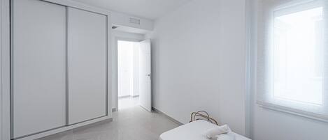 Ein schlicht eingerichtetes Schlafzimmer mit Bett, Kleiderschrank und Fenster.
