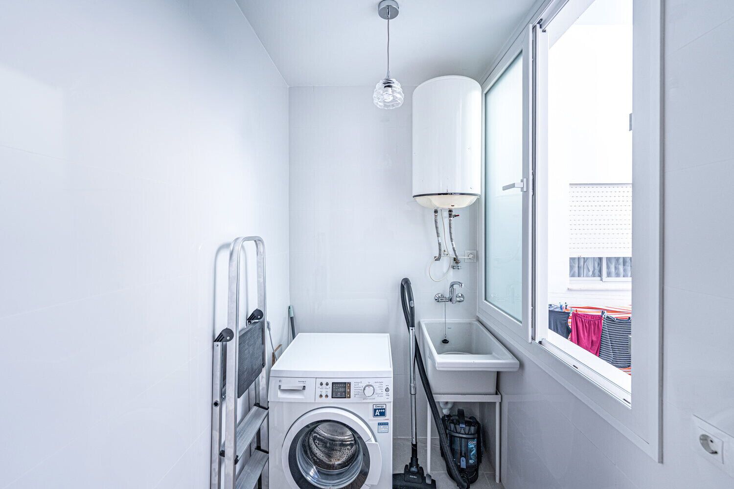 Une petite buanderie équipée d’un lave-linge, d’un évier et d’une douche.