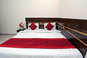 A neatly made bed with a red blanket, white pillows, and a wooden headboard. - Hotel Visa (New Delhi)