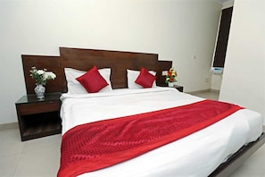 A hotel room with a bed, a nightstand, a vase with flowers, and a mirror. - Hotel Visa (New Delhi)