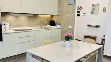 Una cocina moderna con armarios blancos, horno empotrado y comedor con mesa y sillas.