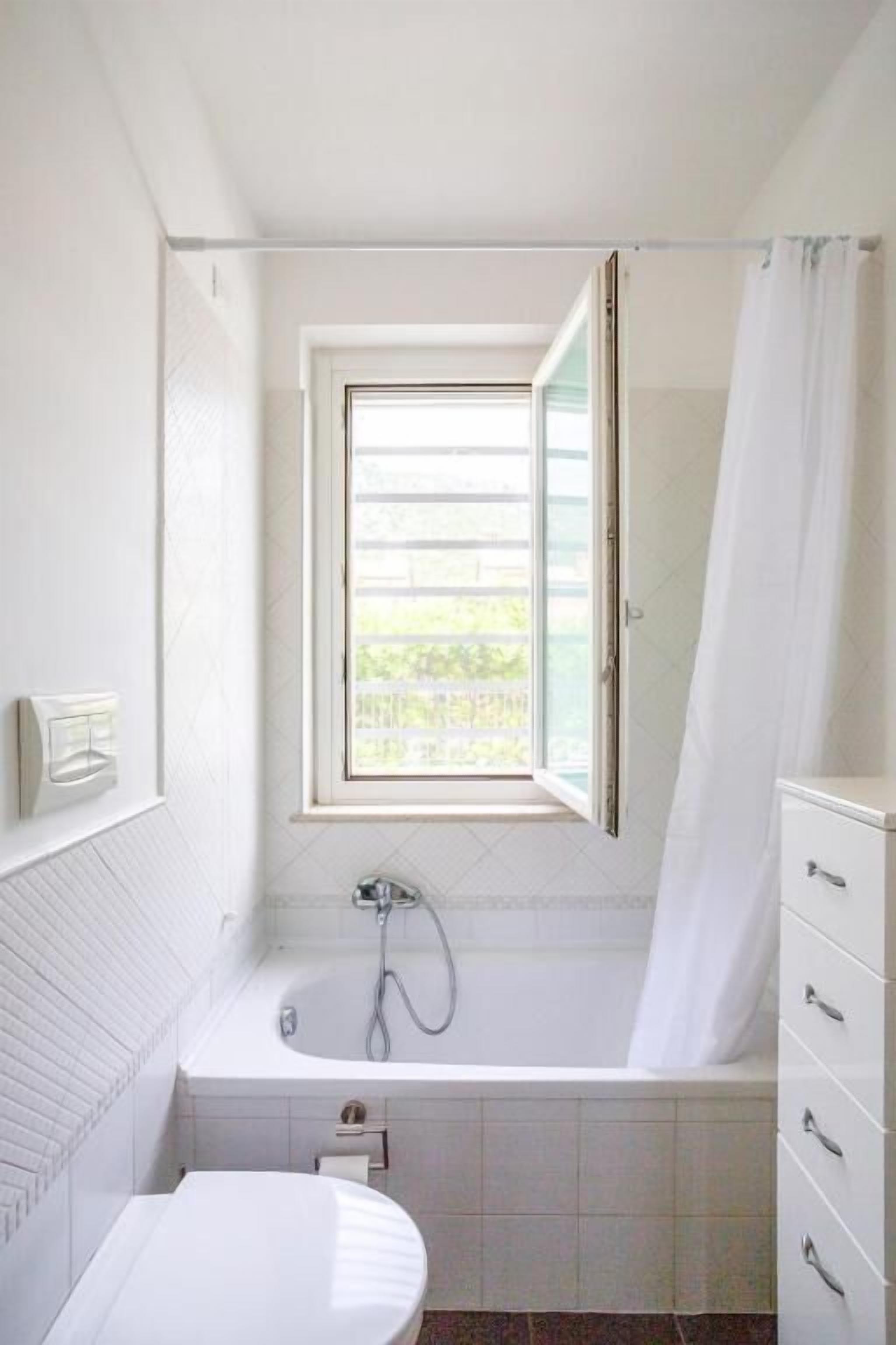 Un baño con bañera, ventana y retrete.