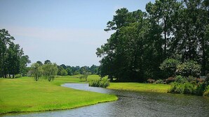 Uma paisagem ribeirinha tranquila com gramado, árvores e um corpo d'água calmo.